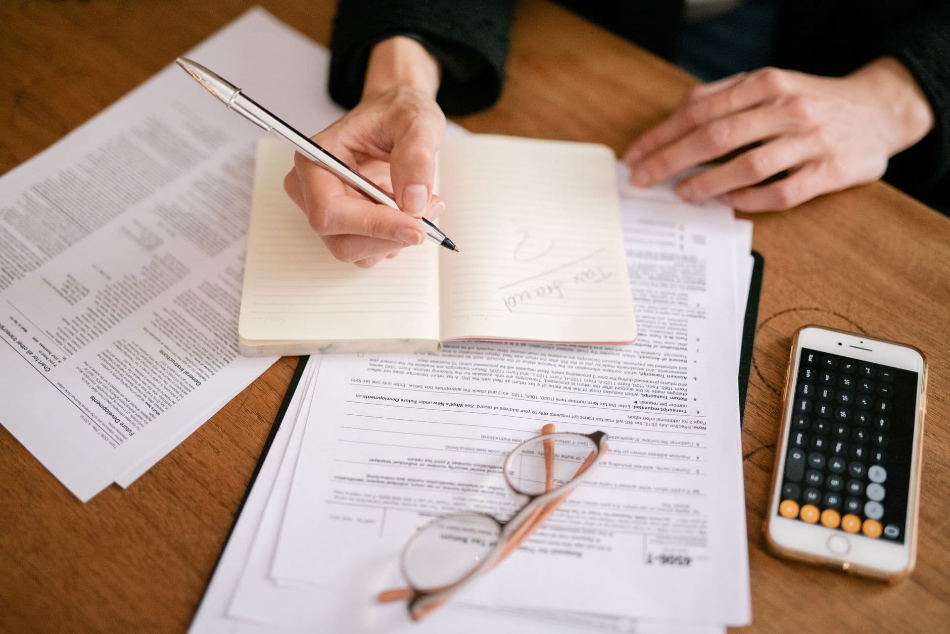Como consultar notas emitidas no seu CNPJ de forma simples Close-up of a person writing in a notebook with documents and a calculator, managing finances.