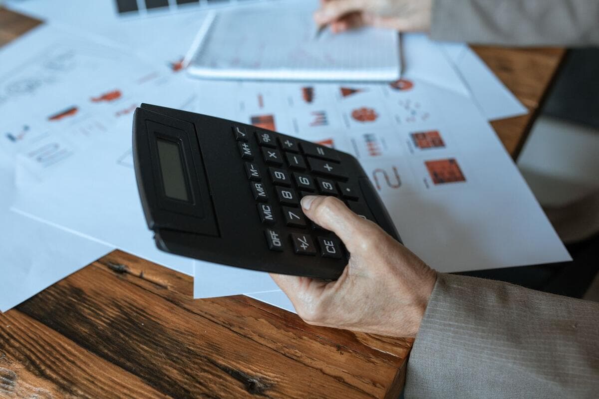 Mão usando calculadora sobre a mesa com gráficos, calculando a retirada do sócio
