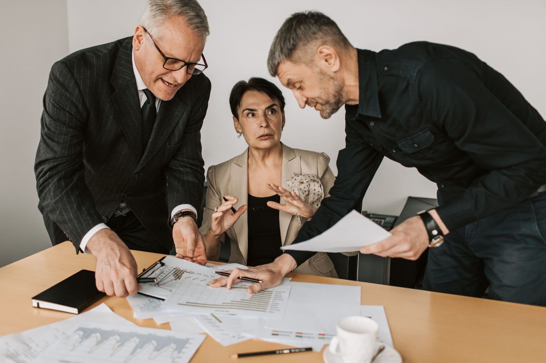 Reforma tributária: checklist para sua empresa revisar Three adults engaged in a dynamic discussion at an office table, analyzing documents and planning strategies.