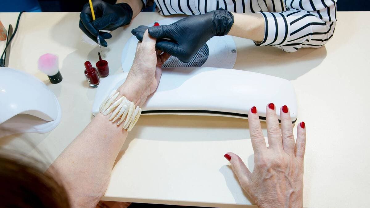 Manicure aplicando esmalte vermelho em sessão no salão